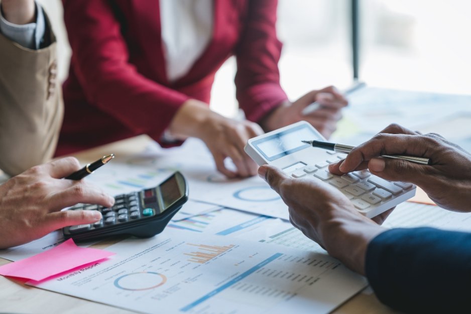 Professionals reviewing charts and spreadsheets while using calculators during a collaborative financial reporting meeting.