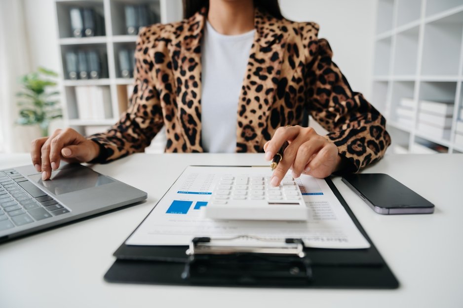Person calculating finances at a desk with a laptop and reports, representing professional monthly bookkeeping services.